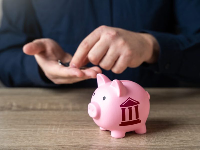 A man putting coins into a piggy bank with a federal building symbol on it.