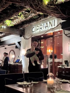 man standing and carrying a baby with cipriani sign behind