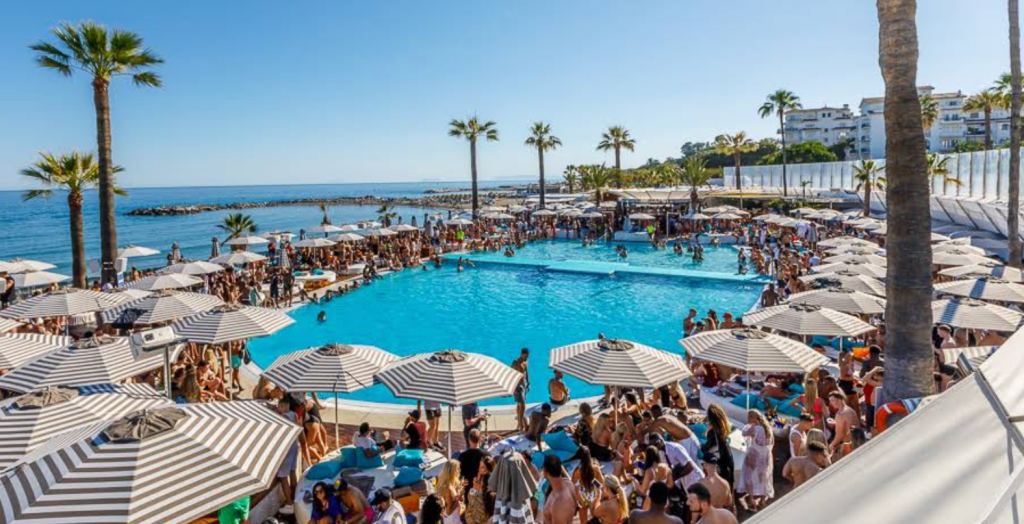 Big pool club sorrounded by sunbeds infront of the ocean